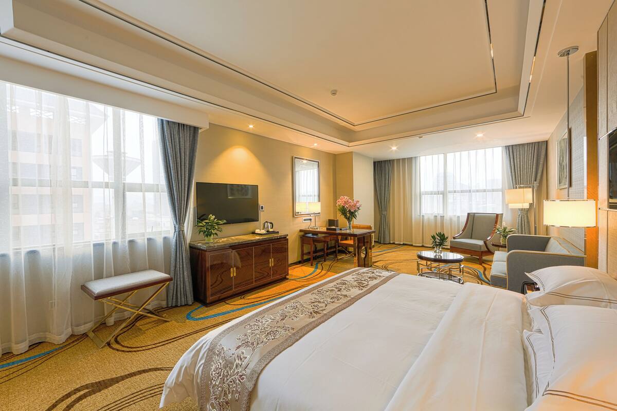 A hotel room with a large bed, a desk, a chair, a television, and a window with curtains.