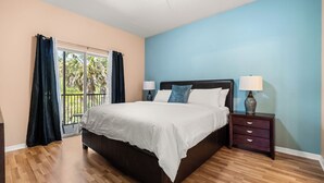 A bedroom with a large bed, a nightstand with a lamp, and a view of the outdoors through a sliding door.
