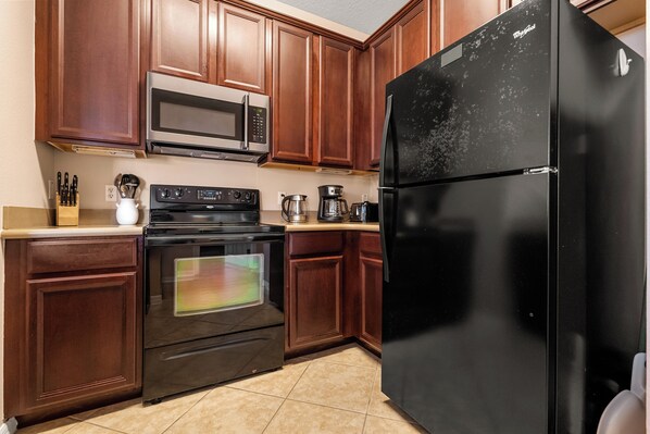 A kitchen with wooden cabinets, a black refrigerator, a microwave, an oven, and a coffee maker.