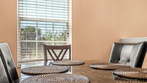 A dining table with woven placemats, black leather chairs, and a window with blinds.