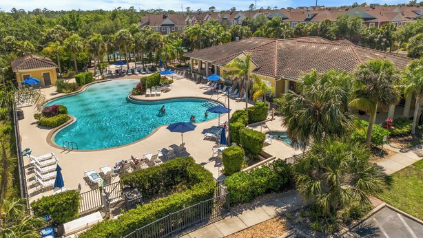 A resort with a large swimming pool, sun loungers, and palm trees.