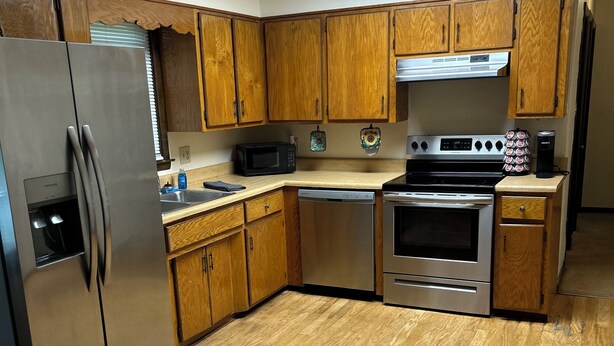 A kitchen with wooden cabinets, stainless steel appliances, and a wooden floor.