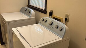A laundry area with two front-loading washing machines and a window with blinds.