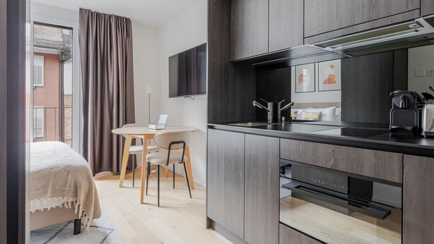 A modern kitchen with dark wood cabinets, a built-in oven, and a flat-screen TV mounted above the counter. - Blueground | Wiedikon, AC & w/d, nr museums (Zurich)