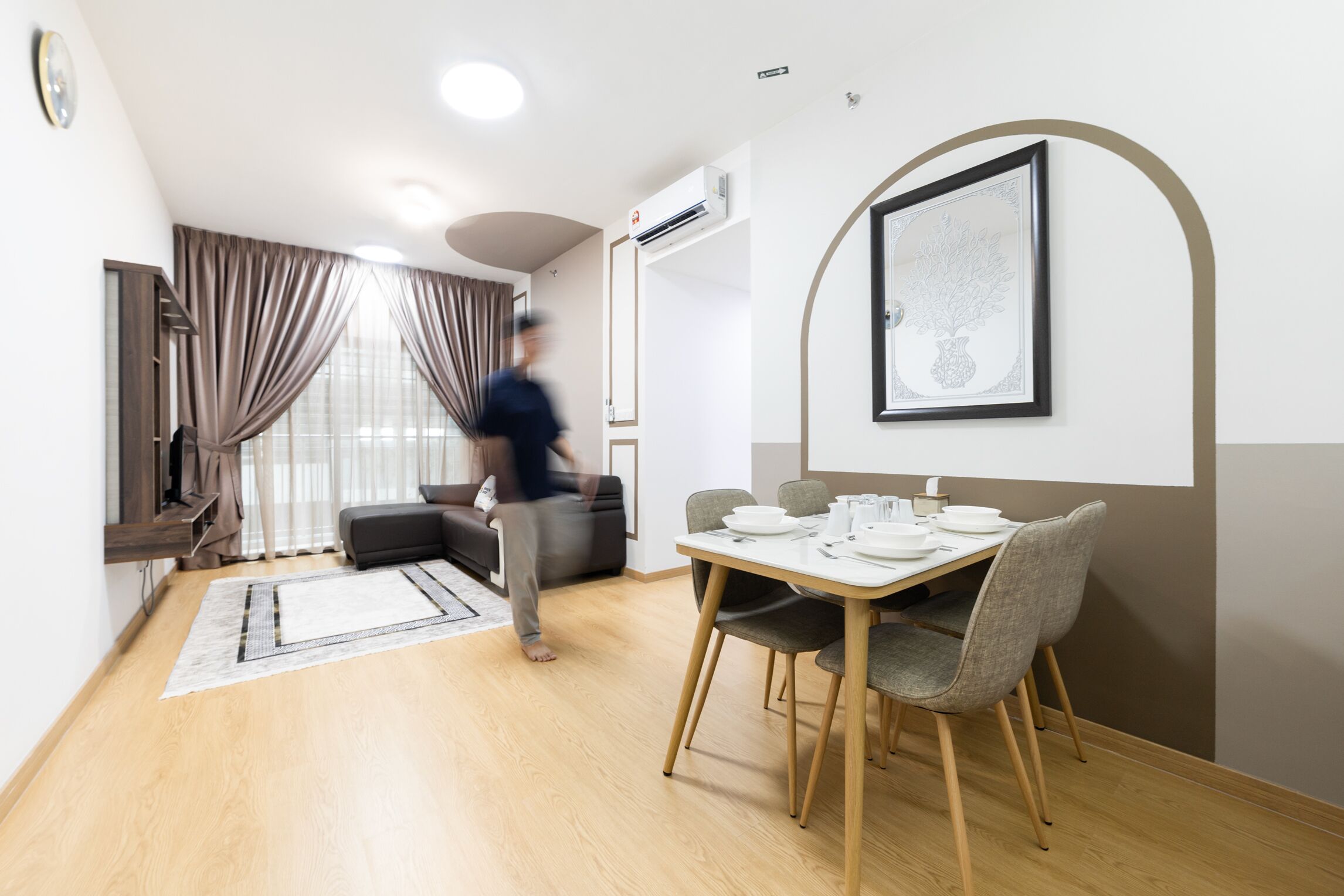 Een moderne woonkamer met een bank, een eettafel gedekt voor twee personen en een groot raam met gordijnen.