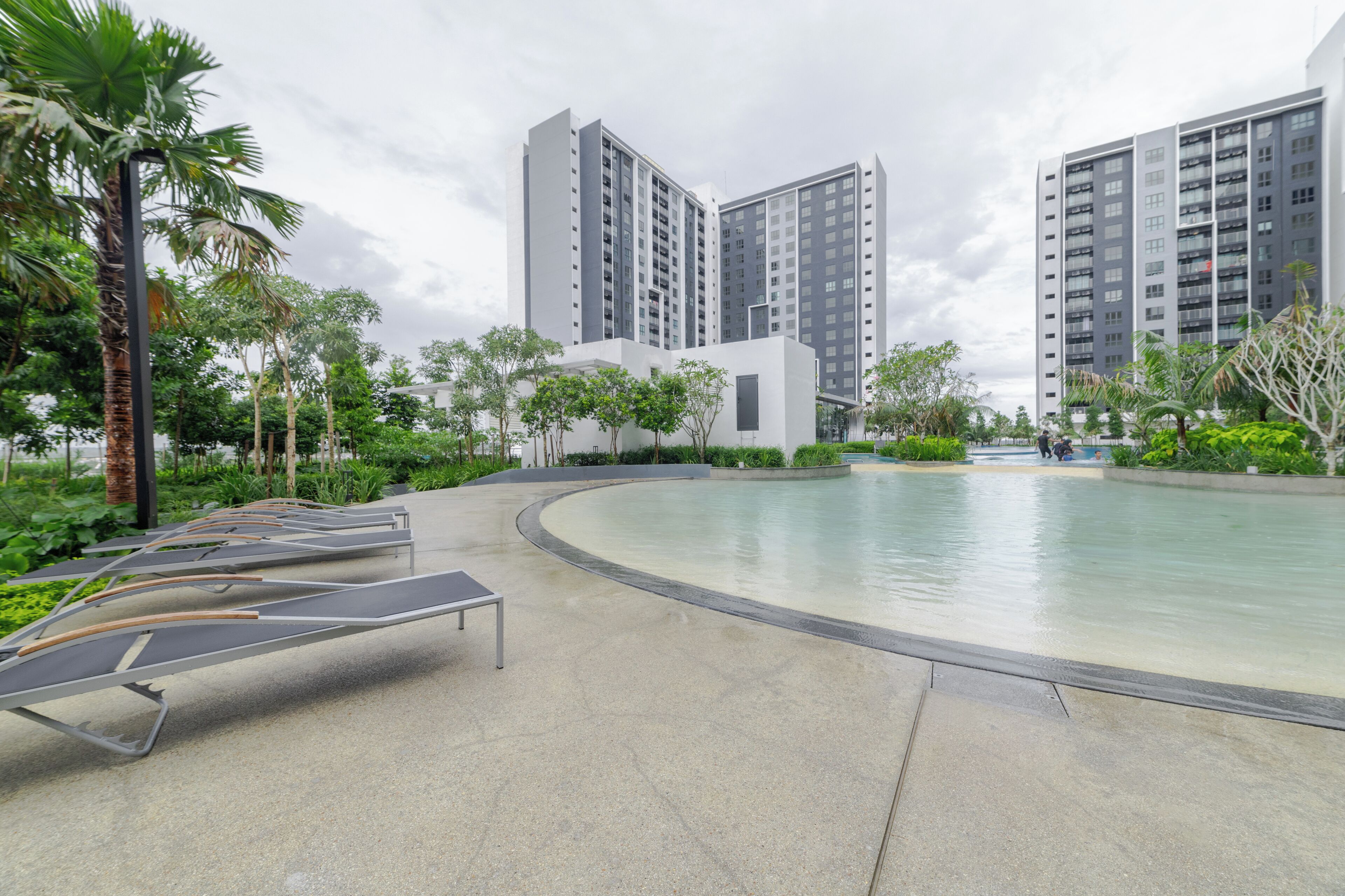 A modern pool area with lounge chairs, surrounded by greenery and tall buildings.