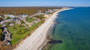 An aerial view of a coastal residential area with houses, a beach, and clear blue water.