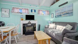 A living room with a fireplace, a television, a sofa, and a dining area with chairs. - SeaGill Rest & Nest - A Peaceful Ocean Hideaway (South Yarmouth)