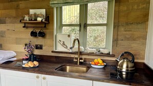 Eine Küche mit Holzrückwand, einem Spülbecken, einem Wasserkocher und einem Fenster mit Blick auf Bäume.