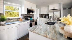 A modern kitchen with white cabinets, a granite countertop, stainless steel appliances, and a window with a view of greenery. - Charming 3-bedroom villa with AC, WiFi in tranquil Naples (Naples)