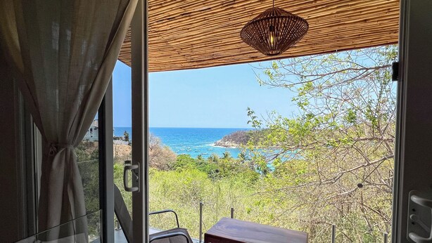Un balcon avec une table et des chaises, offrant une vue sur un paysage côtier avec des arbres et la mer.