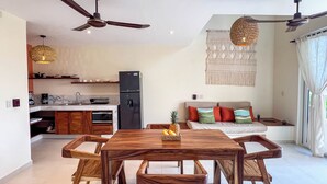 Une cuisine moderne équipée d’un réfrigérateur, d’un four à micro-ondes et de meubles de rangement en bois. On y trouve une table à manger avec des chaises et un panier de fruits.
