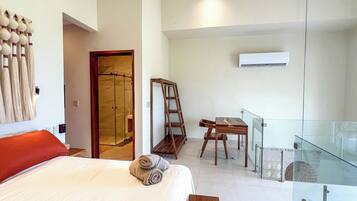 Habitación de hotel moderna con cama, escalera de madera, barandilla de vidrio y zona de ducha.