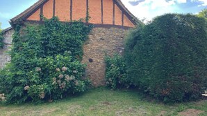 Un edificio de piedra con tejado a dos aguas, parcialmente cubierto de hiedra, rodeado de abundante vegetación.