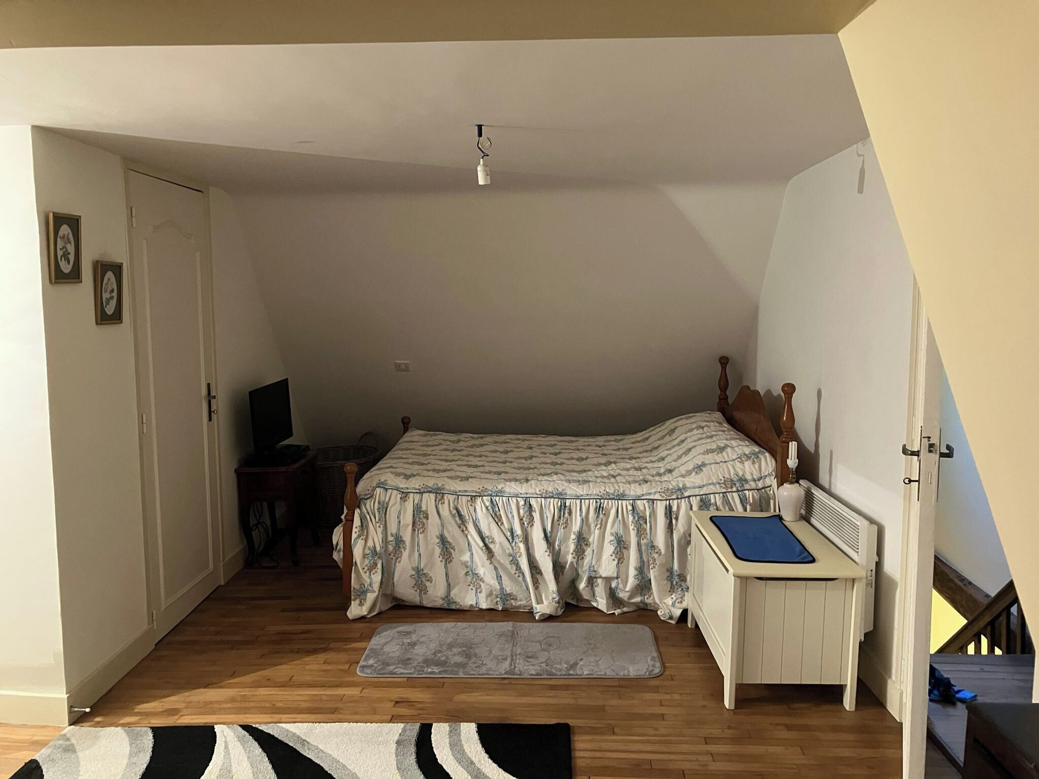 Ein Schlafzimmer mit Bett, Schreibtisch, Stuhl, Heizkörper und einer Treppe.