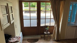 Una cocina con un lavamanos, una silla con un florero, y vista de la calle a través de una puerta.