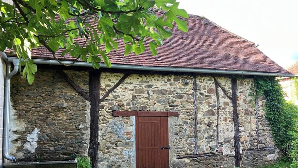 Un edificio de piedra con tejado de tejas rojas, una puerta de madera y un banco de piedra.