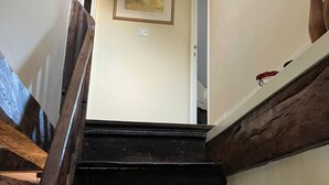 Una escalera con peldaños de madera y barandilla oscura, que lleva a una puerta con interruptor de luz en la pared.