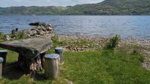 A lakeside view with a stone bench and wooden posts, surrounded by grassy areas and hills. - Farmburn Bothy by Interhome (Invermoriston)