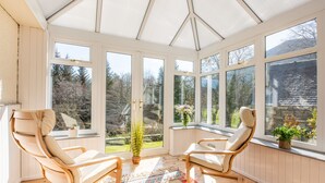 A sunroom with two wooden chairs, a patterned rug, and a view of a garden through large windows. - Farmburn Bothy by Interhome (Invermoriston)