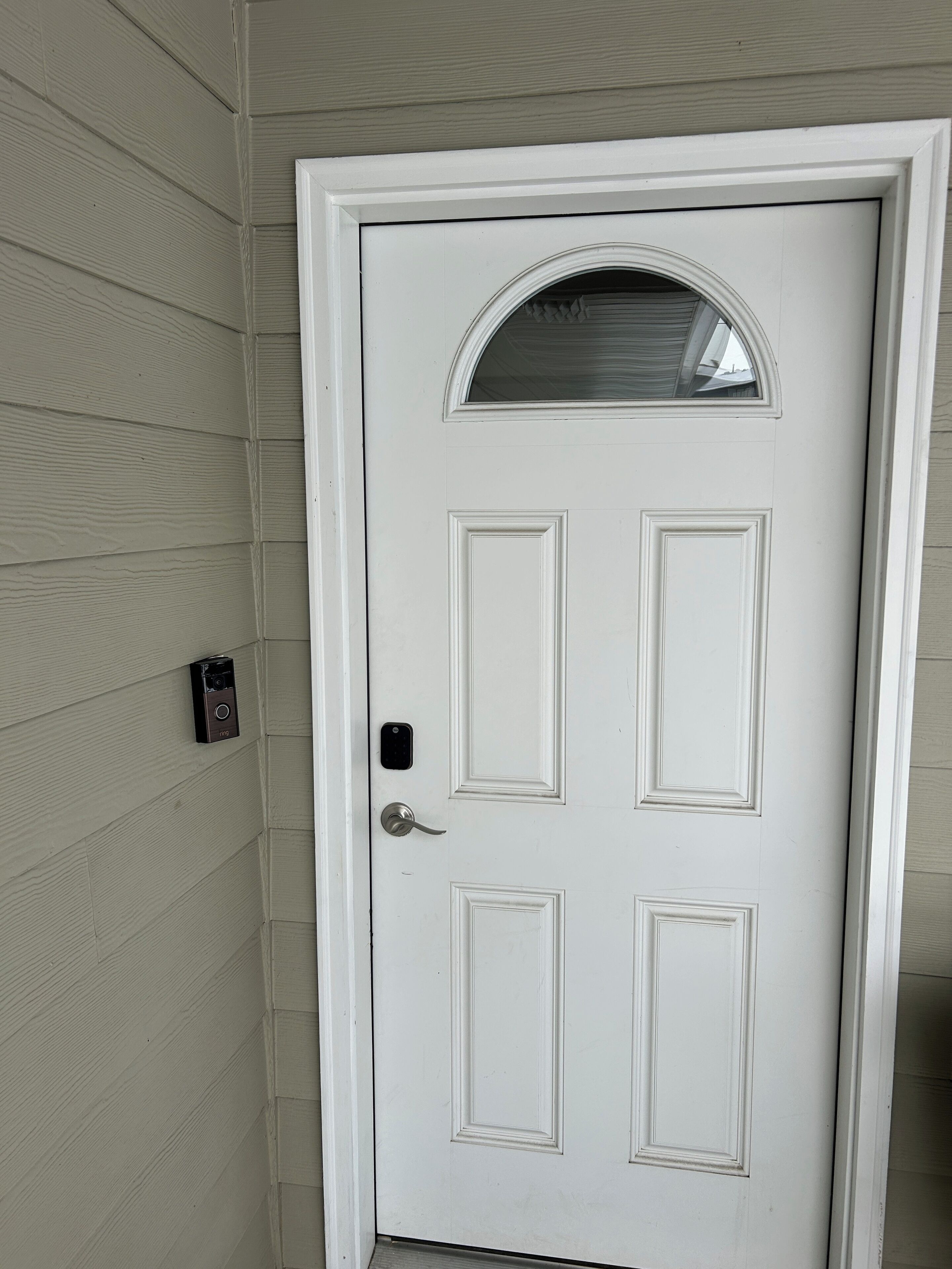 A white door with a small window above it, a doorbell, and a mailbox on the wall.