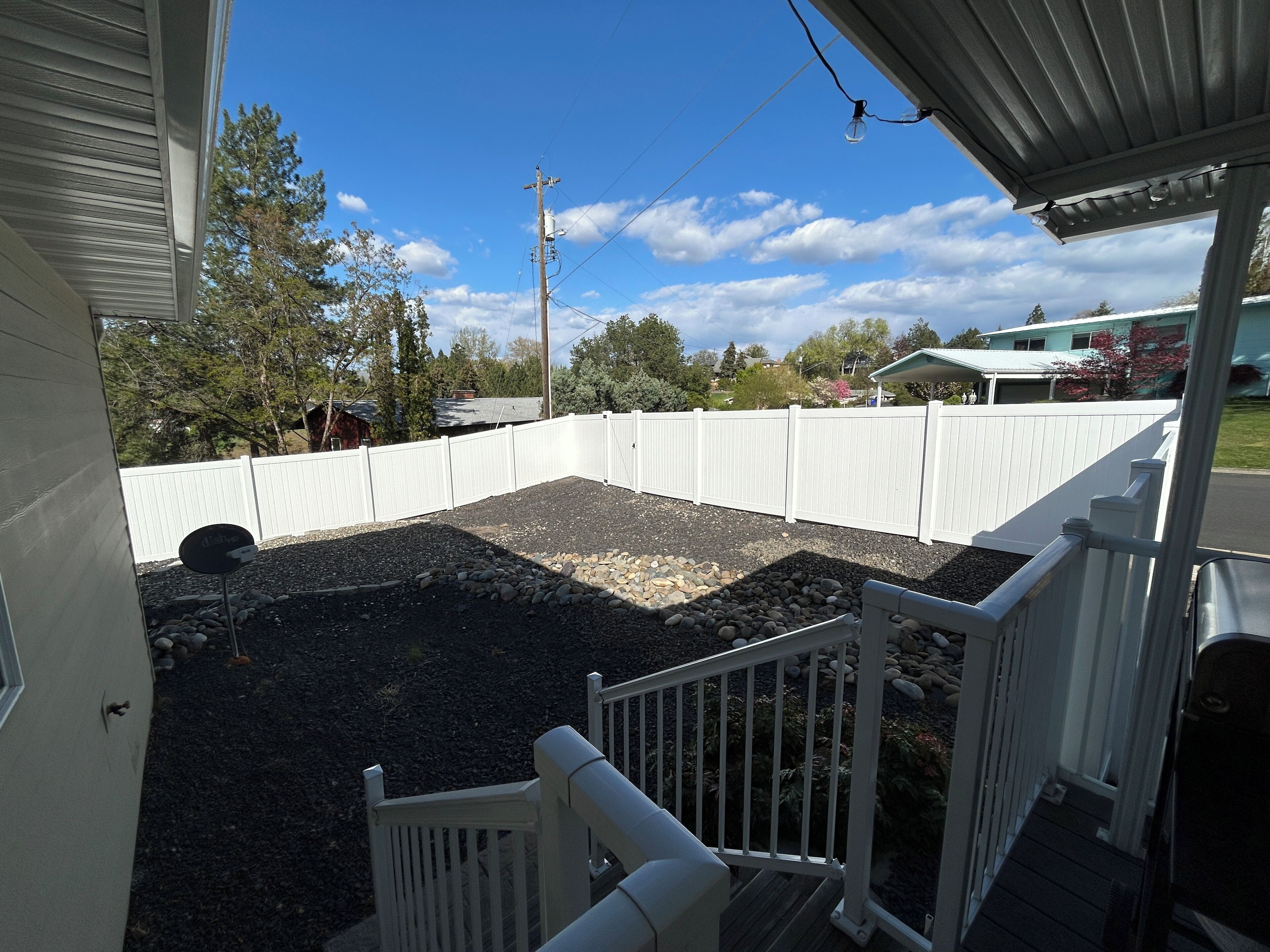 A backyard with a white fence, a wooden deck, and a satellite dish.