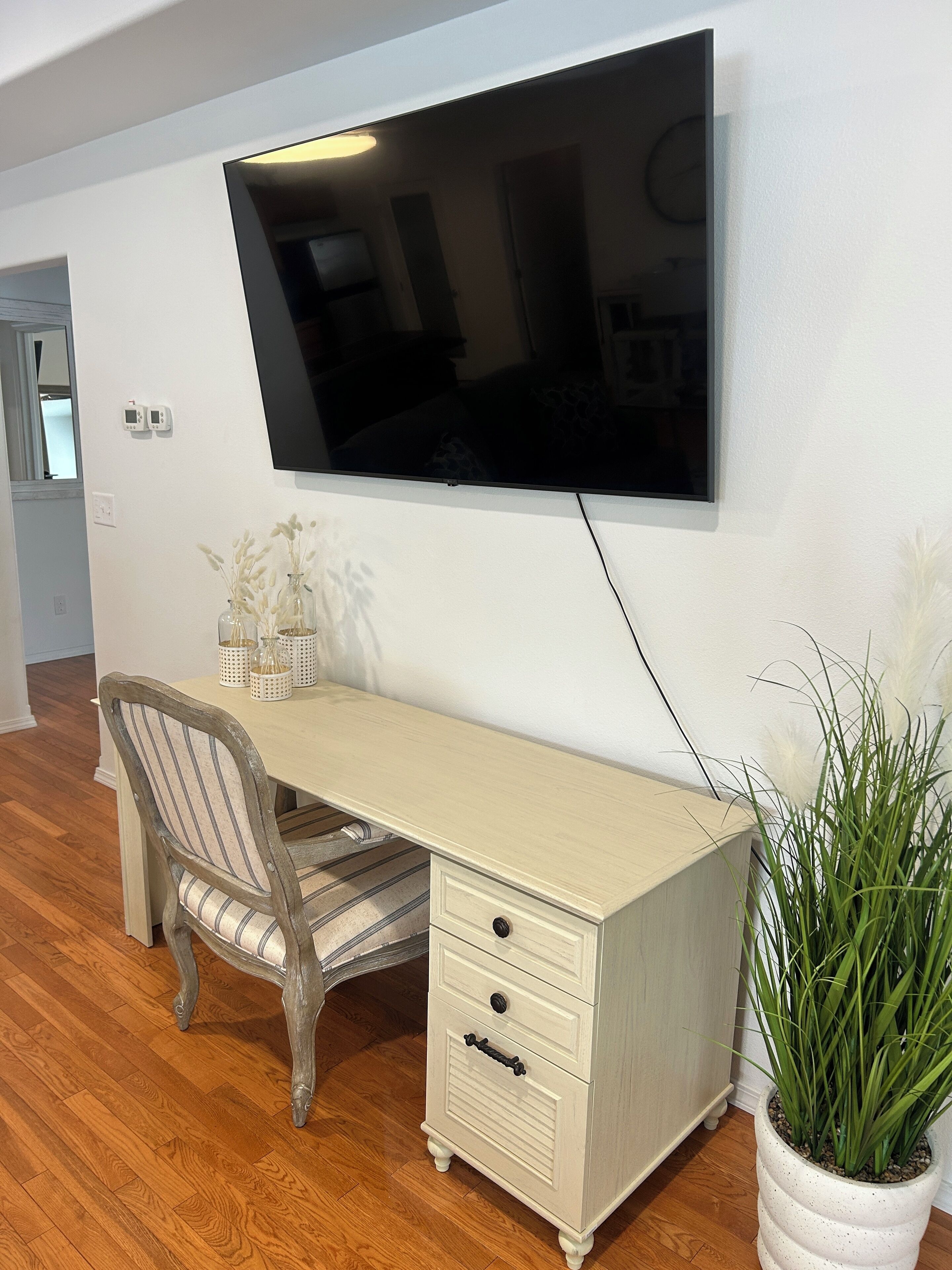 Une chambre moderne avec un grand bureau, une chaise, un téléviseur fixé au mur et une plante en pot.