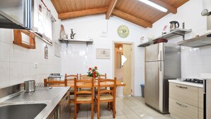 Eine Küche mit Holzkstühlen, einer Edelstahl-Spüle, einem Kühlschrank und einem Esstisch mit Blumen in einer Vase.