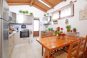 Une cuisine avec une table et des chaises en bois, un réfrigérateur, un four, un four à micro-ondes et diverses plantes en pot.