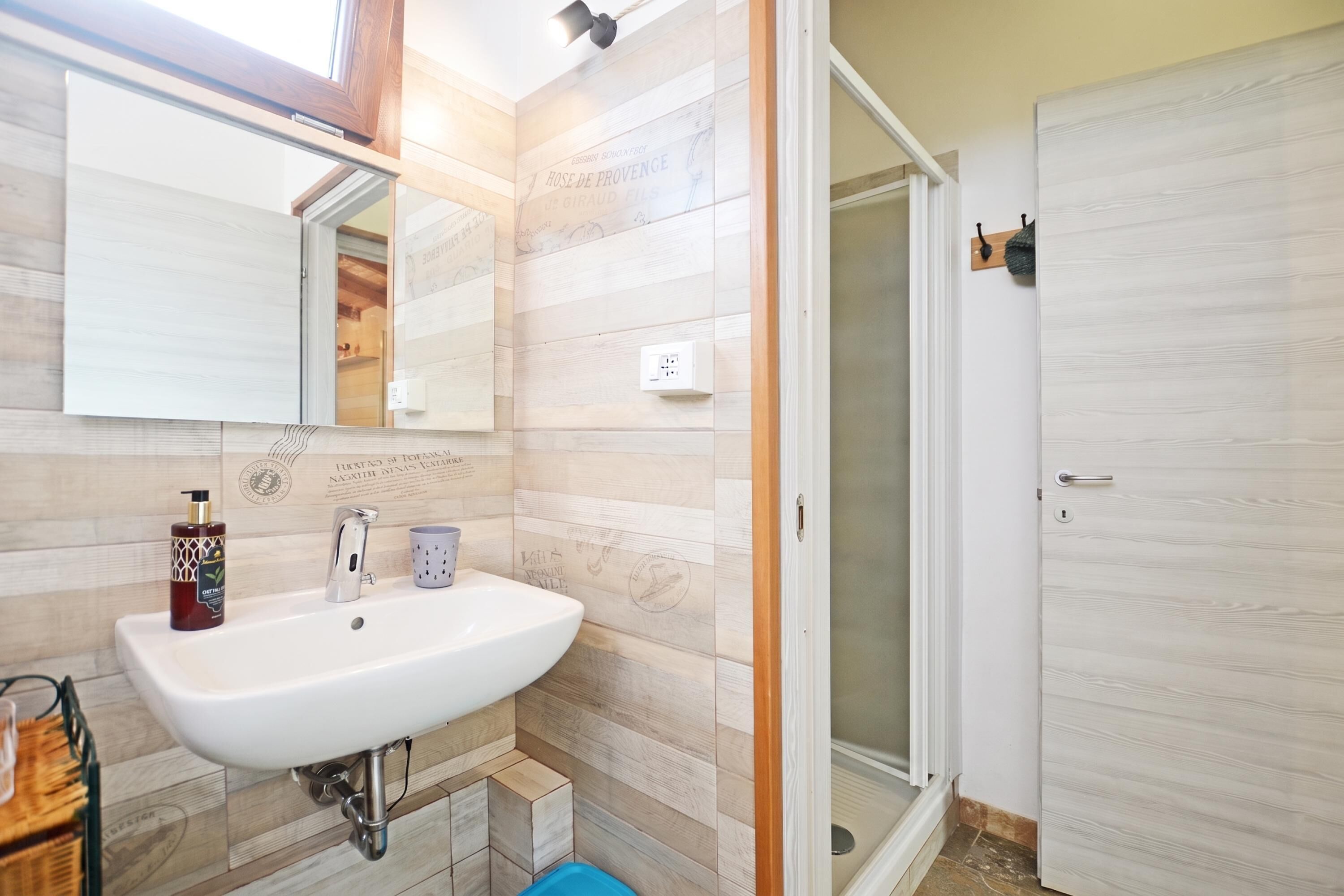 A bathroom with a white sink, a mirror, a shower with a glass door, and wooden wall panels.