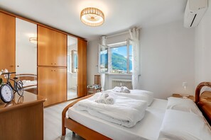 Hotellihuone, jossa on sänky, puinen vaatekaappi, peili, polkupyörä ja näkymä vuorille.