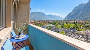 Een balkon met een tafel en stoelen, met uitzicht op een stadsgezicht en bergen in de verte.