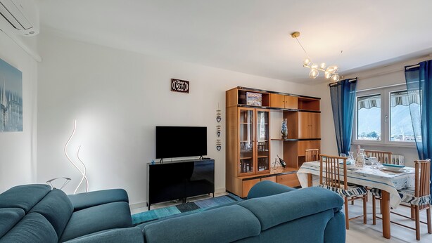 Een moderne woonkamer met een bank, televisie en een eethoek met een tafel en stoelen.