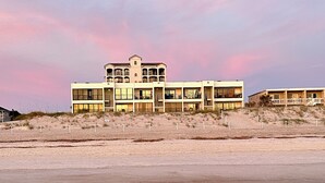 Ein Strandhotel mit mehreren Etagen, Balkonen und einem Sandstrand im Vordergrund.