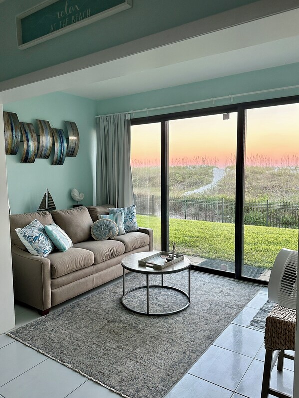A modern living room with a sofa, coffee table, and a view of a green landscape through large windows.