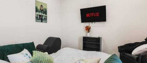 A bedroom with a bed, a chair, a TV mounted on the wall, and a small table with a vase.