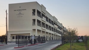 Un edificio de varios pisos con el rótulo "The International Apartments", una entrada con portón y un área de estacionamiento.