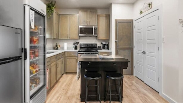 Una cocina moderna con refrigerador, microondas, estufa y taburetes de bar.