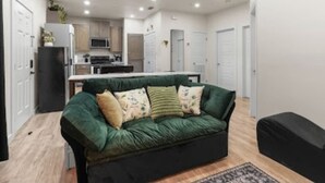 Una sala de estar moderna con un sofá verde, un reposapiés negro y una cocina al fondo.