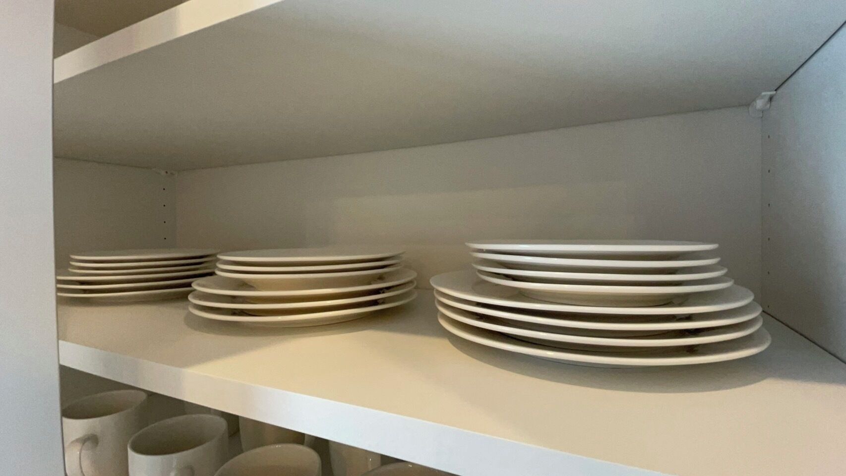 Una estantería blanca con pilas de platos blancos.
