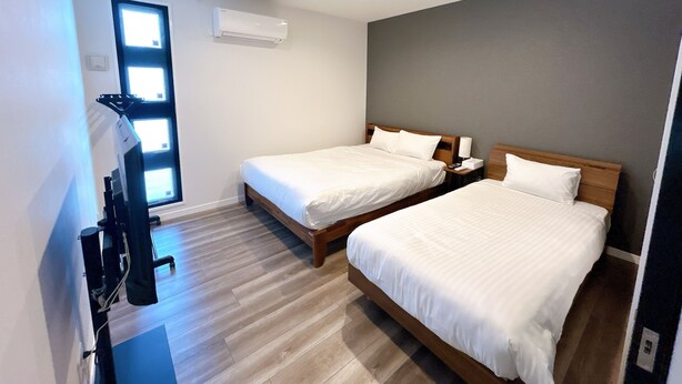 Une chambre d’hôtel avec deux lits, une fenêtre, un appareil de climatisation et un plancher en bois.