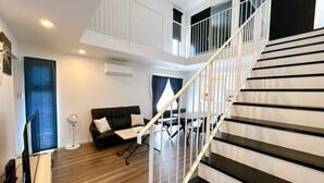 Un salon moderne avec un canapé noir, une petite table et un escalier doté de rampes blanches.