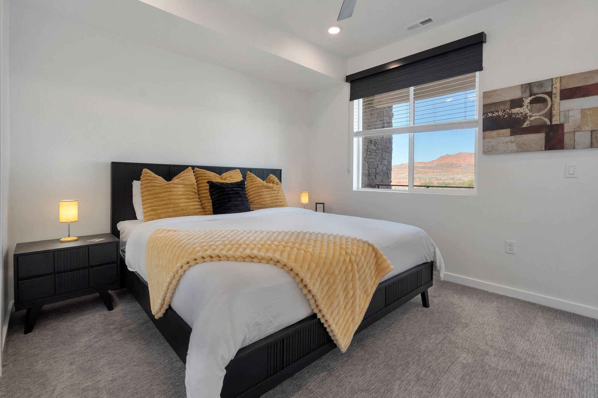 A bedroom with a bed, nightstands, a window with a view, and a wall-mounted artwork.