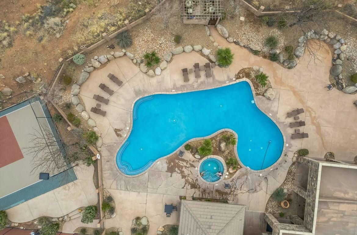 An aerial view of a swimming pool area with a large pool, a smaller circular pool, and surrounding lounge chairs and seating areas.