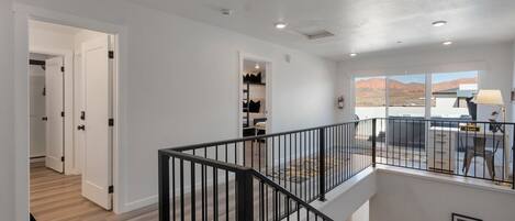 A spacious room with a high ceiling, a staircase, and a view of a mountainous landscape through large windows.