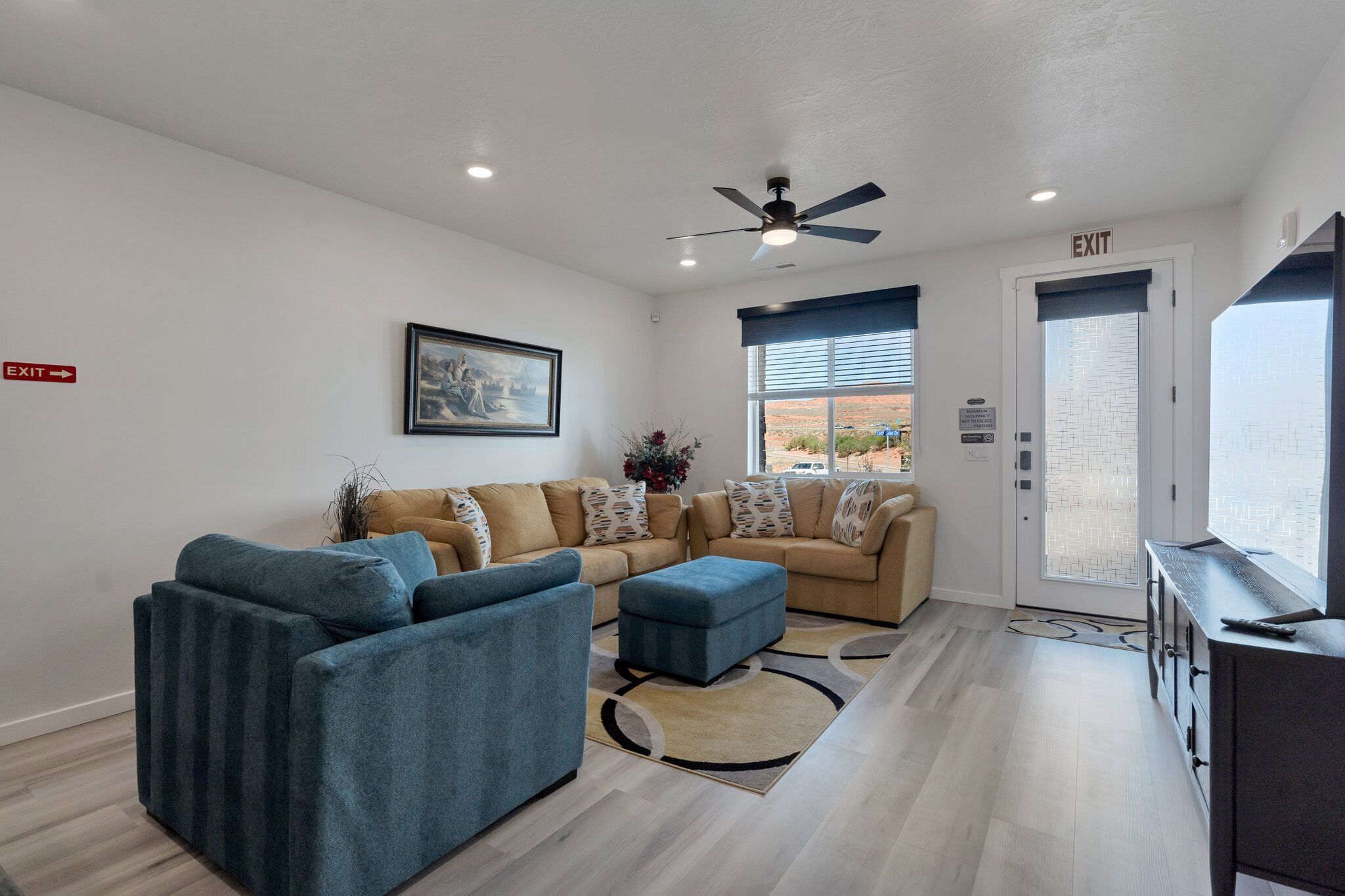 A modern living room with a beige sofa set, a blue armchair, and a ceiling fan.