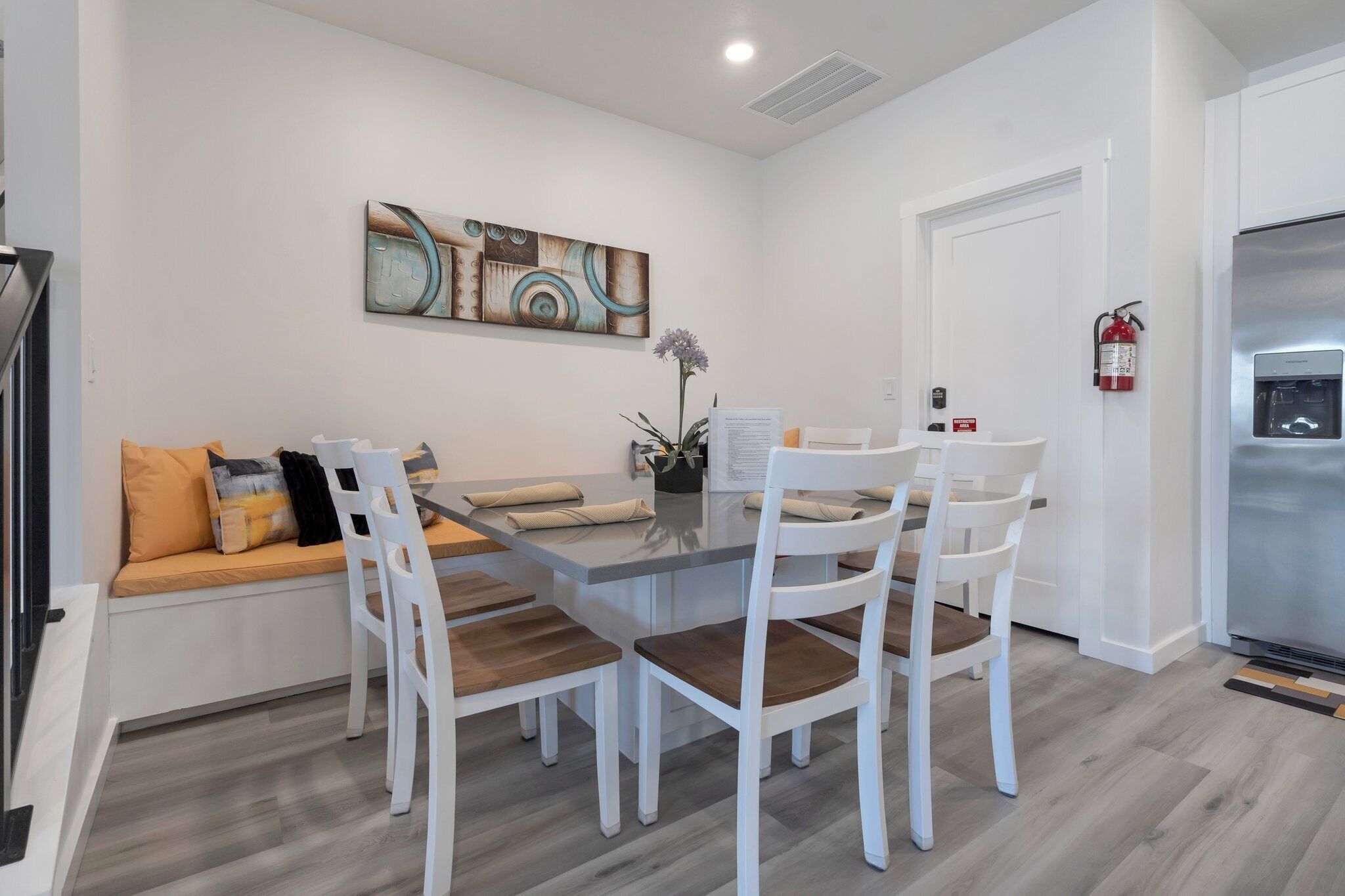 A modern kitchen with a stainless steel refrigerator, white cabinetry, and a dining area with a glass table and white chairs.