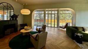 A spacious living room with a fireplace, a large arched window, and a green sofa. - Dream villa 50 meters from the beach! (Benerville-sur-Mer)