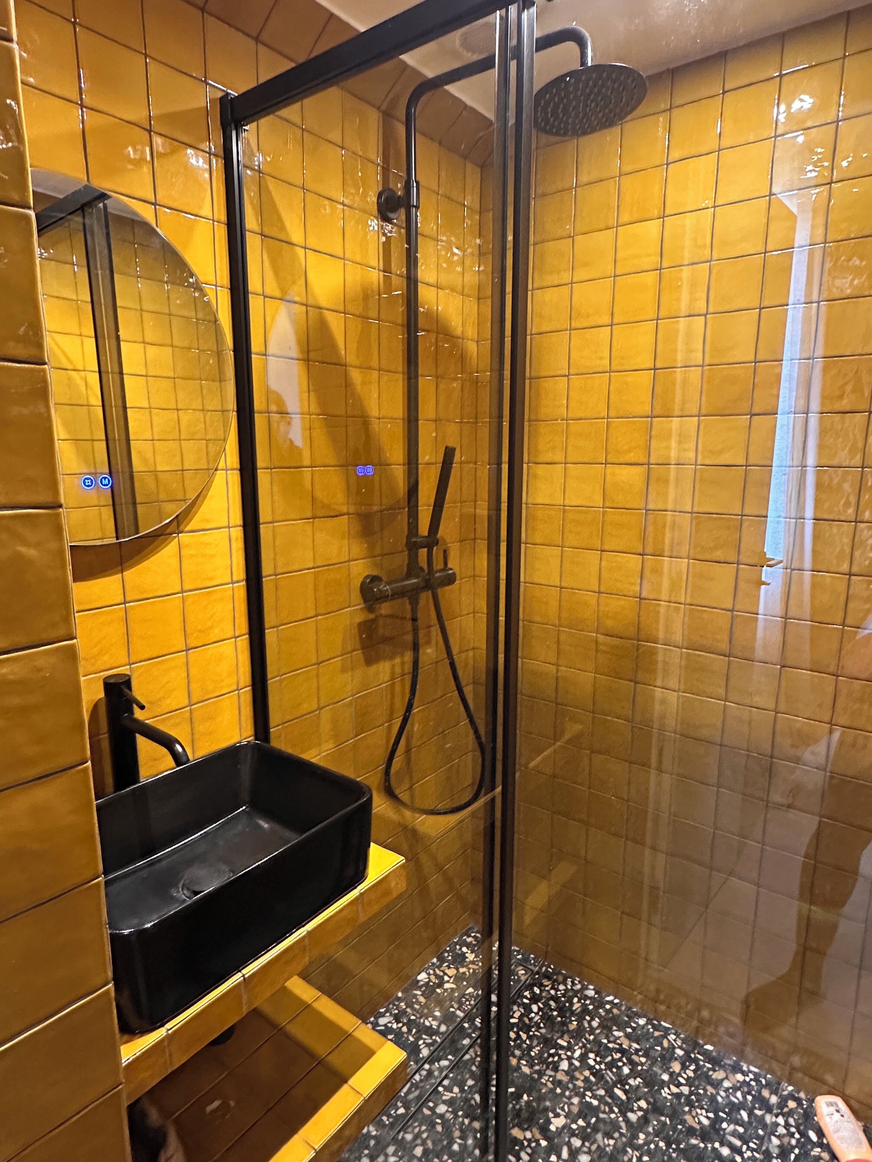 A glass-enclosed shower stall with a black sink and a handheld showerhead.