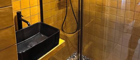 A glass-enclosed shower stall with a black sink and a handheld showerhead.